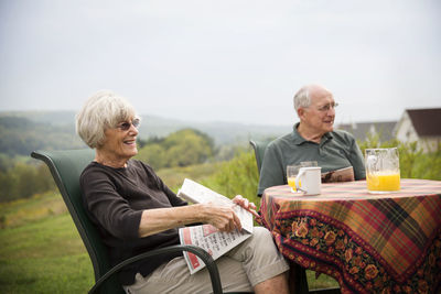 Senior couple sitting at table on field against sky