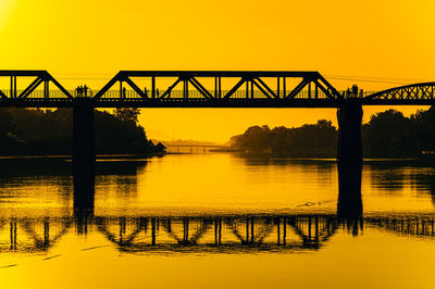 Silhouette bridge over river against sky during sunset