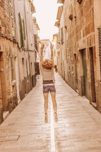 Rear view of woman jumping over road amidst buildings