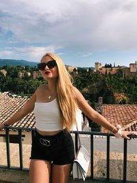 Young woman wearing sunglasses standing against built structure