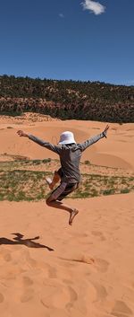 Rear view of boy leaping dramatically into the air on a coral pink sand dune landscape 