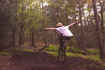Full length rear view of teenage boy riding bicycle in forest