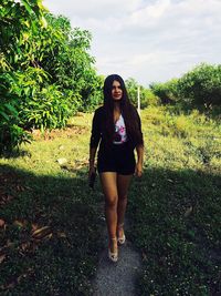 Full length of young woman standing on grass against sky