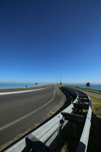 Road by sea against clear blue sky