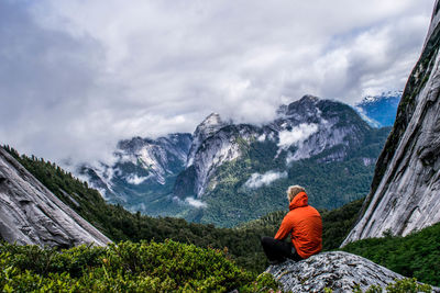 Rear view of male hiker sitting on mountain against cloudy sky