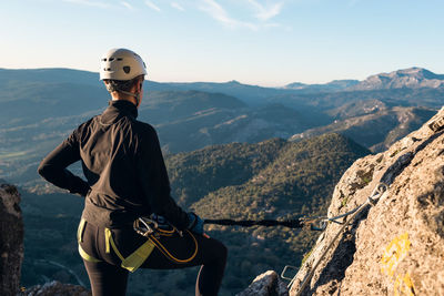 Concept: adventure. climber woman with helmet and harness. from the back looking at the natural landscape of andalusia. secured to the natural wall with a carabiner. via ferrata in the mounta