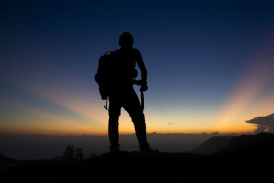 Silhouette young man standing on mountain against sky during sunset