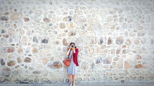 Woman photographing on footpath against wall