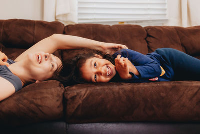 Smiling mother and daughter lying on sofa at home
