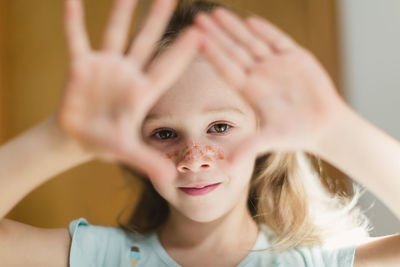 Little girl with glitters on face gesturing while looking at camera in blur