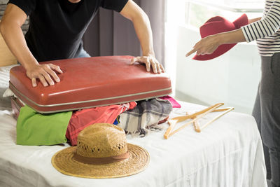 Midsection of man packing clothes in suitcase by woman gesturing at home