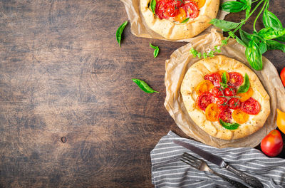 Fresh homemade galettes with tomatoes, ricotta cheese and basil on rustic plywood background. 