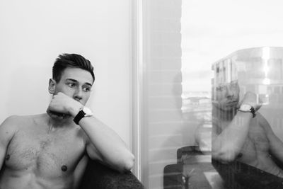 Thoughtful shirtless man siting on sofa by window at home