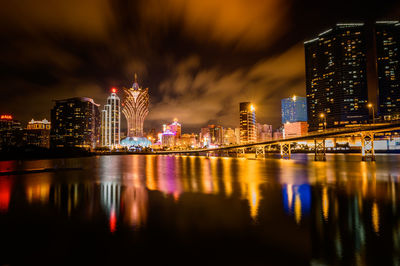 Illuminated buildings by river against sky at night