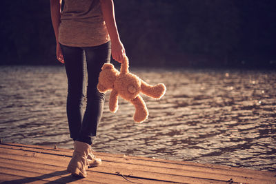 Low section of woman with teddy bear walking at lakeshore