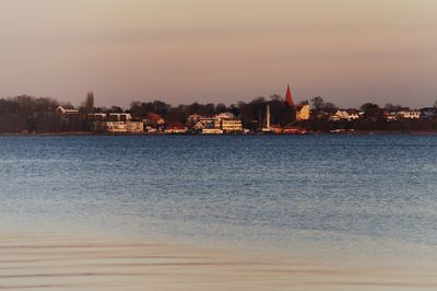 Sea by buildings against sky during sunset