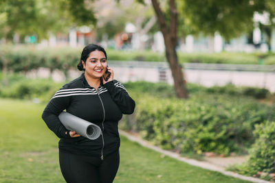 A young indian woman with a sports mat in her hands is walking from a workout in the fresh air