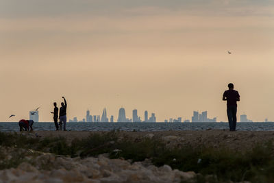 Rear view of men standing on beach against sky during sunset