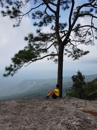 Man sitting on tree by mountain against sky