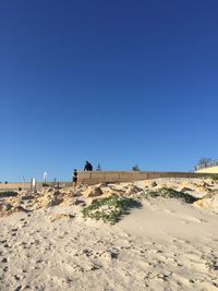 People walking on sand dune against clear blue sky