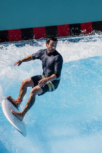 Male athlete surfing with surfboard on wave in swimming pool