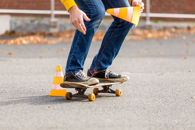 Low section of man holding traffic cone while skateboarding on road