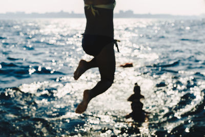 Low section of woman jumping on beach against sky