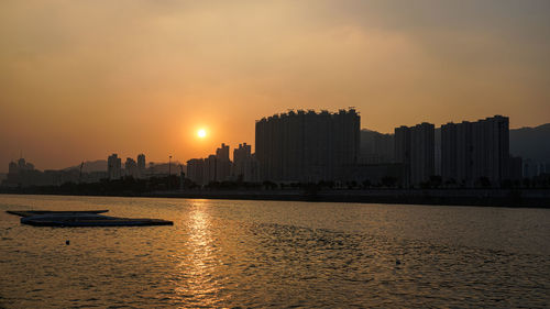 Sea by buildings against sky during sunset