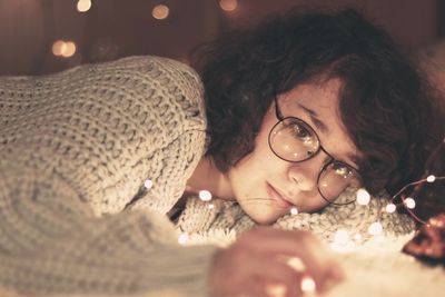 Woman with illuminated string lights lying in home