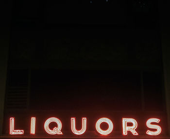 Illuminated liquors neon sign against clear sky at night
