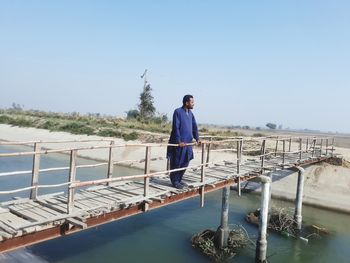 Man standing by railing against sea against clear sky