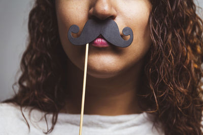 Midsection of woman holding mustache against wall