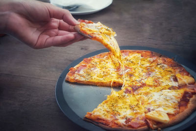 Cropped image of hand holding pizza on table