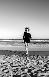 Full length of woman standing on beach against clear sky