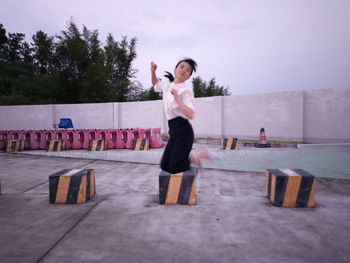 Young woman jumping on street against sky