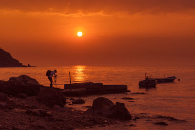 Man photographing at beach against sky during sunset