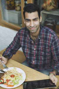 Portrait of smiling man using digital tablet while having lunch at cafe