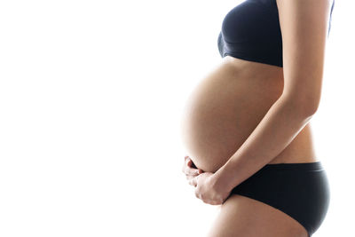 Midsection of pregnant woman standing against white background