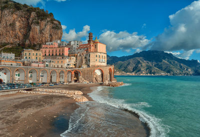 View of buildings by sea against cloudy sky