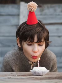 Birthday boy in grey knitted sweater with dark short hair blows candle on the birthday cake