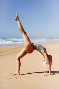 Woman exercising at beach against sky