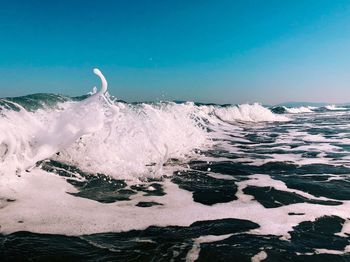 Waves splashing on shore against clear blue sky