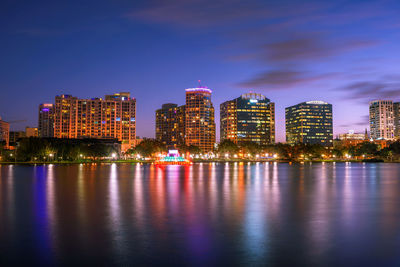 Illuminated buildings by river against sky at night