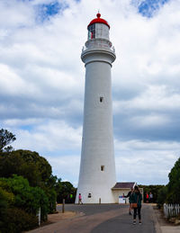 People on lighthouse by building against sky