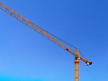 Low angle view of crane against clear blue sky