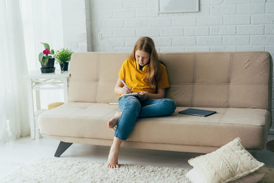 Full length of girl writing while sitting on sofa