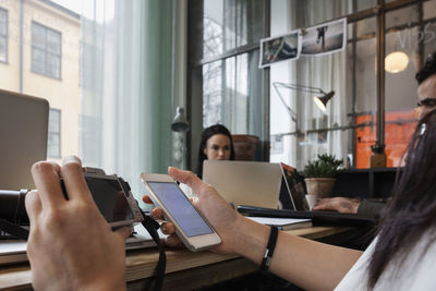 Close-up of blogger holding camera and smart phone while sitting at table in office