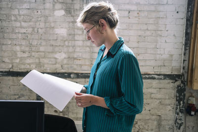 Confident young female it professional reading document standing at creative workplace