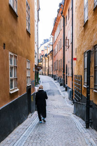 Rear view of woman walking at alley amidst buildings
