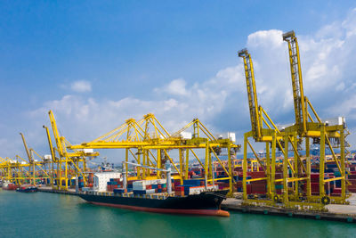 Cranes at commercial dock and shipping containers blue sky background 